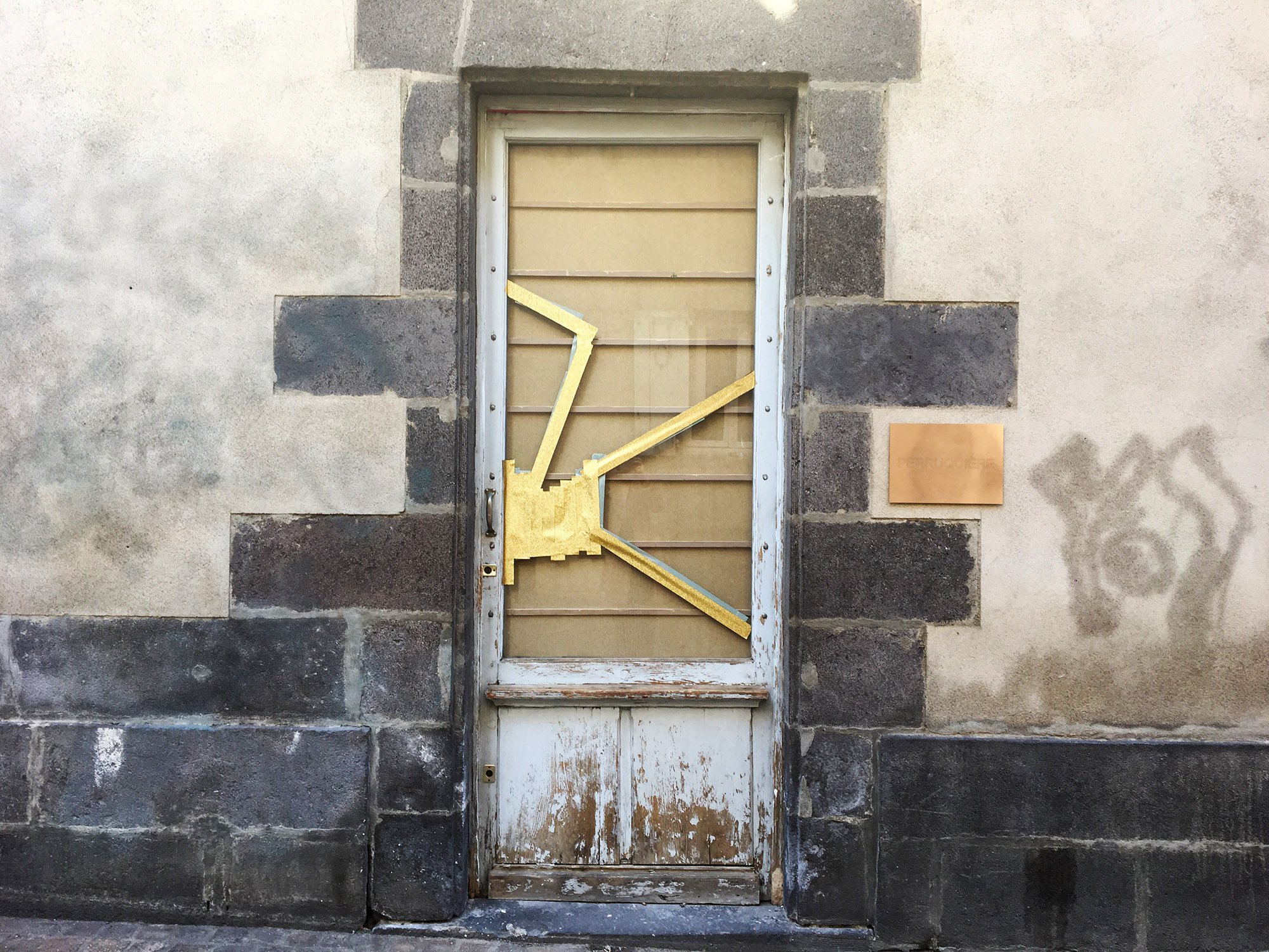 Une porte d'entrée d'un  batiement dont la vitre semble cassée. Un scotch doré recouvre les fissures.